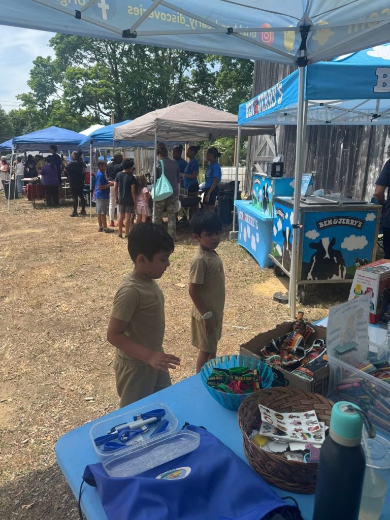 Children browse items at blue-clothed tables during an outdoor fair.