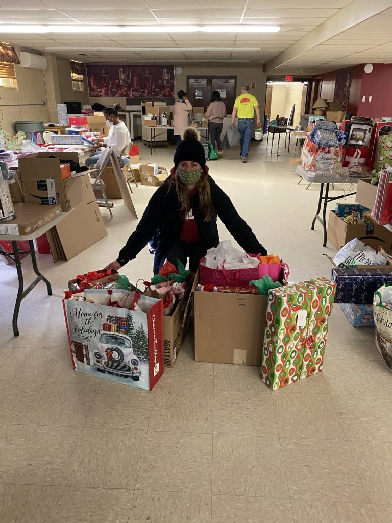 A woman organizes large gift bags and boxes indoors for a giveaway.
