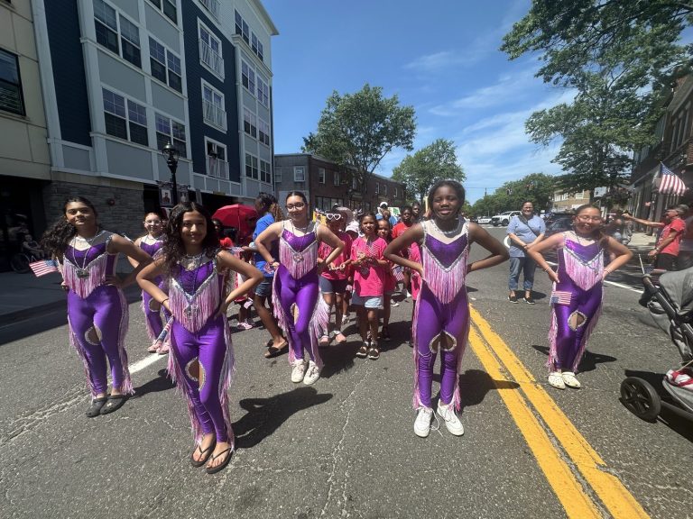 Girls in purple and pink parade outfits walk together down a street.