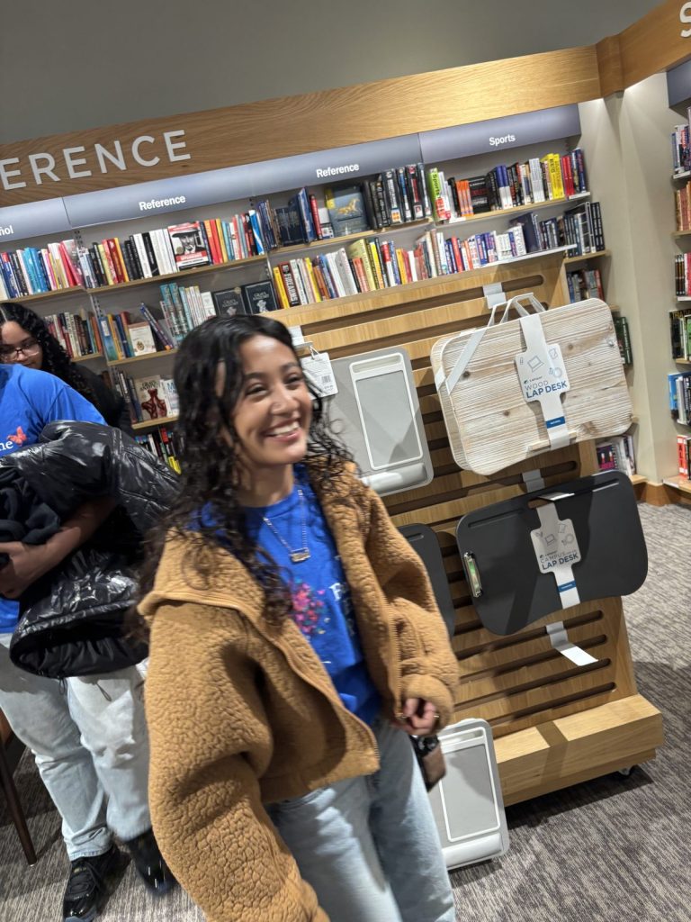 A young woman in a blue Butterfly Effect shirt laughs in a bookstore aisle.