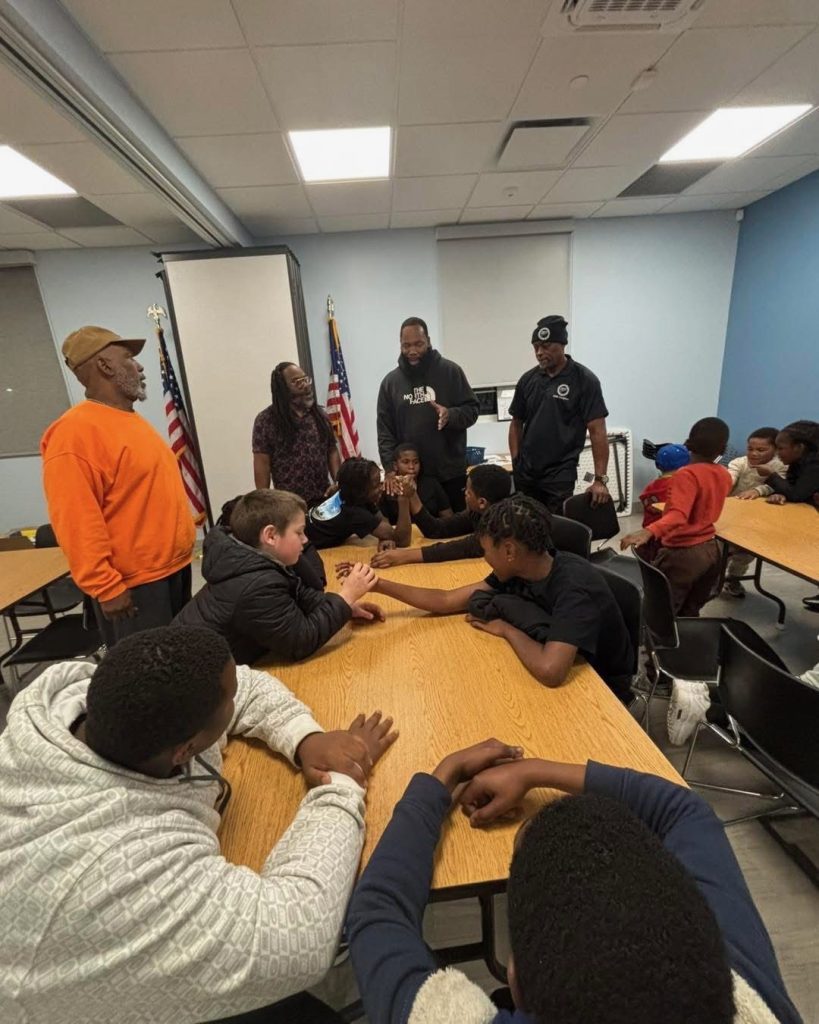 Youth and adults squeeze into a tight group huddle hug indoors.