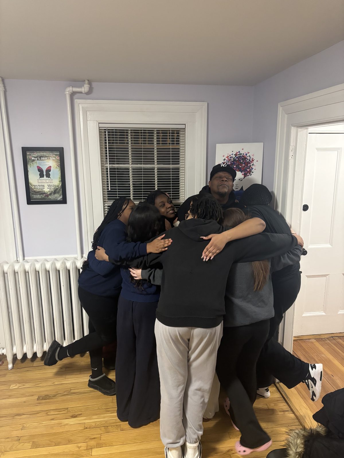 Youth and adults squeeze into a tight group huddle hug indoors.