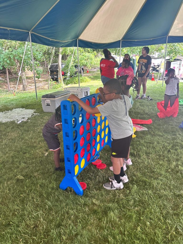 Children play giant Connect Four at a BEP community event under a tent