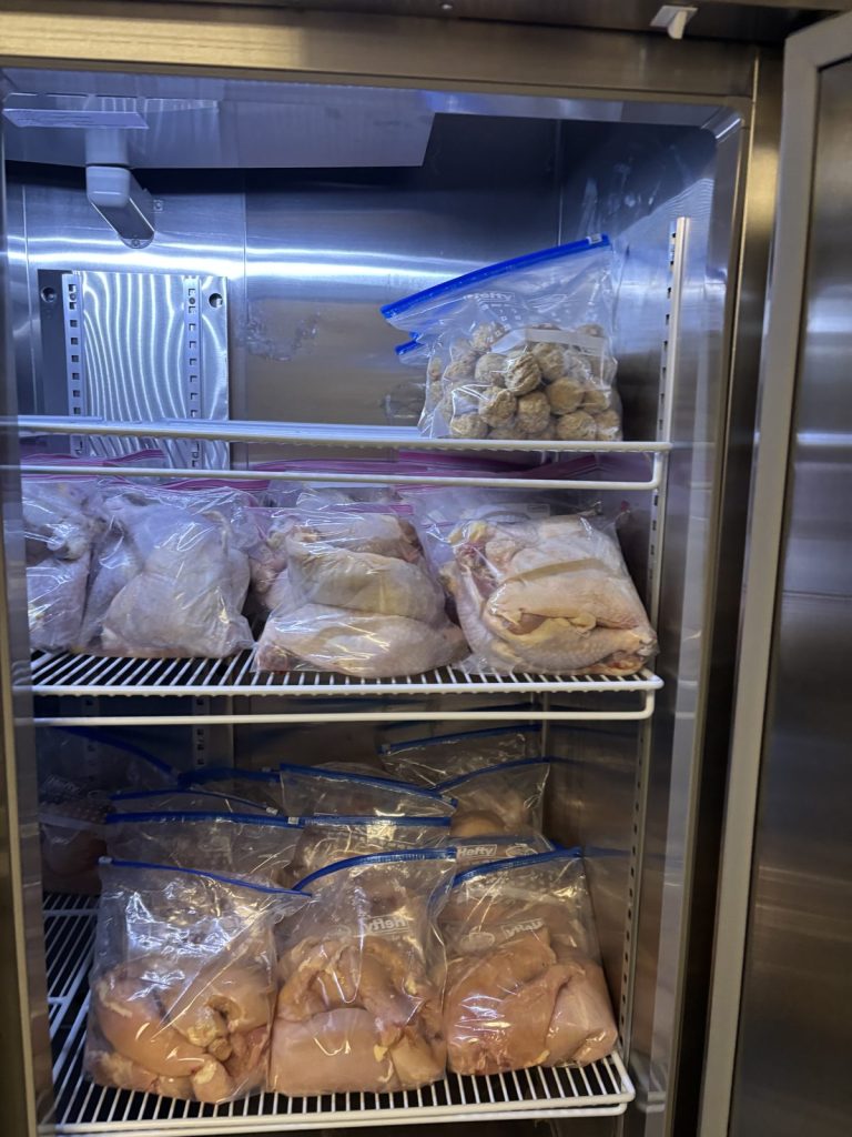 An organized commercial freezer drawer holds labeled bags of food ready for families.