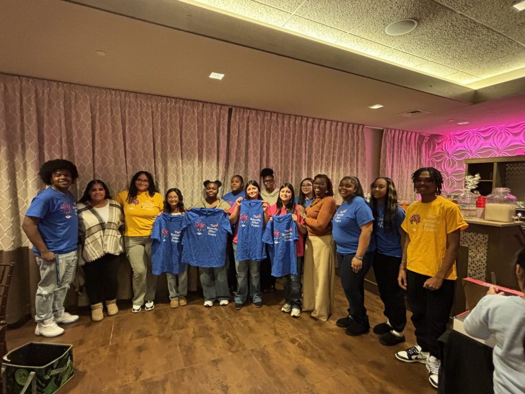 A large indoor group of youth and adults includes blue Butterfly Effect shirts and yellow tees.