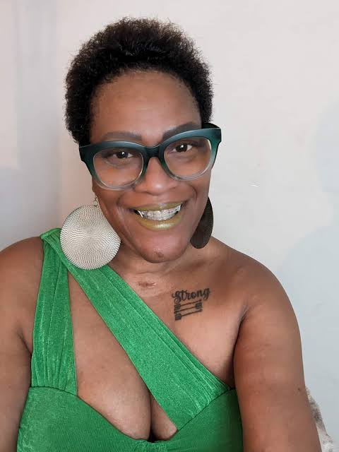 Edna White smiles in a portrait, wearing a bright green top and cat-eye glasses.